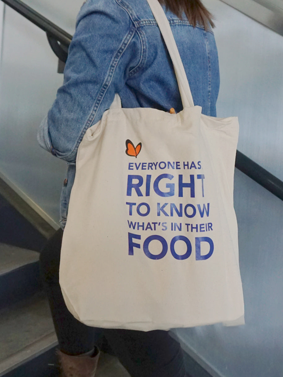 Woman carrying Non-GMO Project tote on shoulder, tote back has quote "Everyone has a right to know what's in their food"