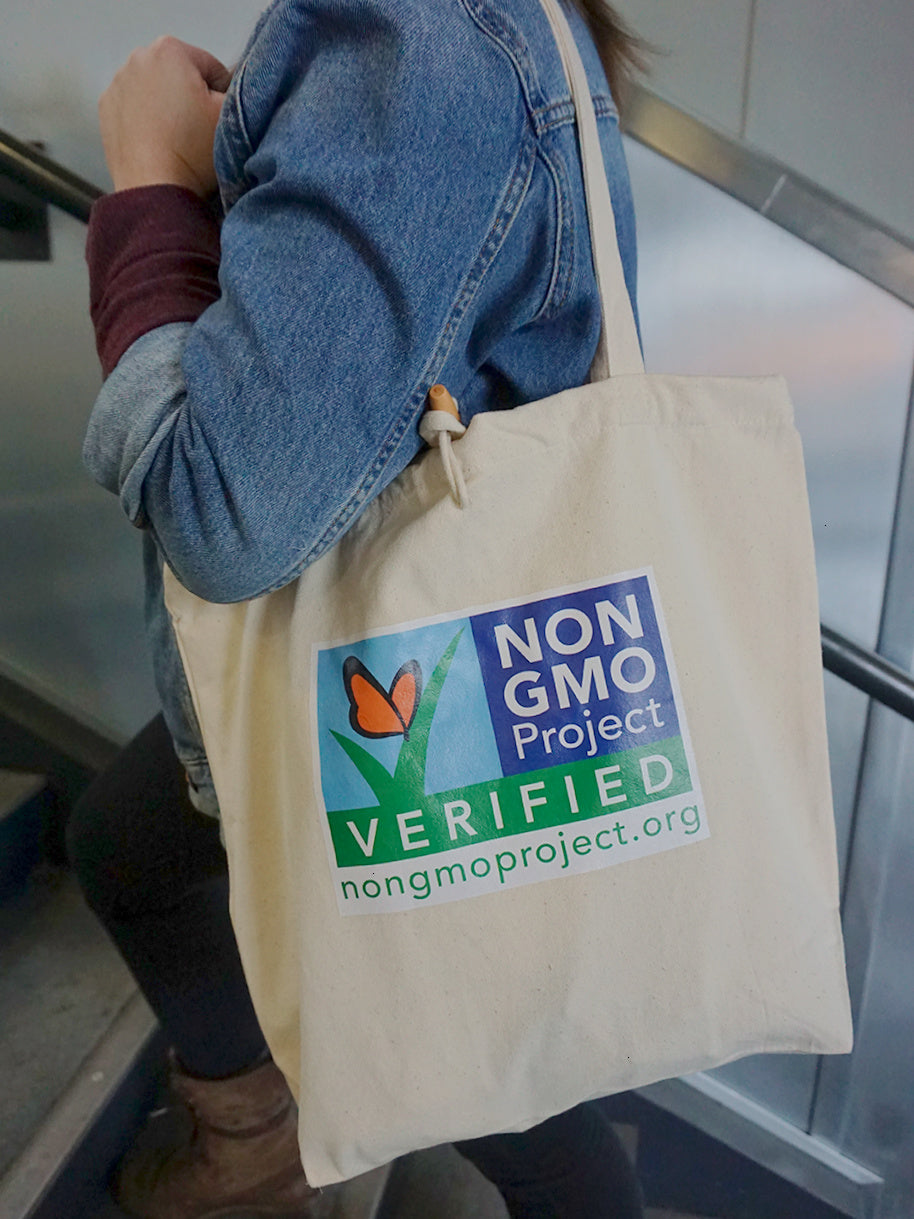 Woman carrying Non-GMO Project tote on shoulder,  the front of the tote has the Non-GMO Project logo