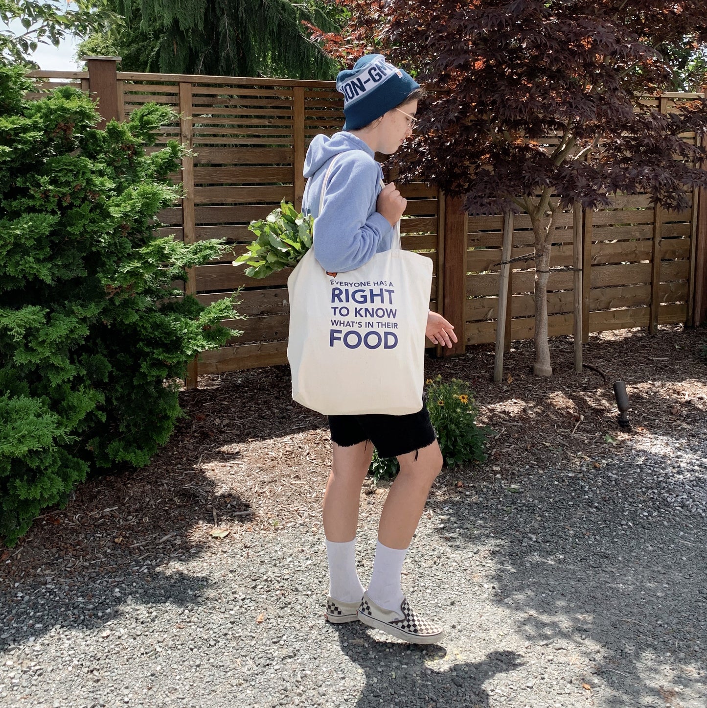 Person with their side to camera, carrying Non-GMO Project  tote on their shoulder and wearing Non-GMO Project beanie on their head.