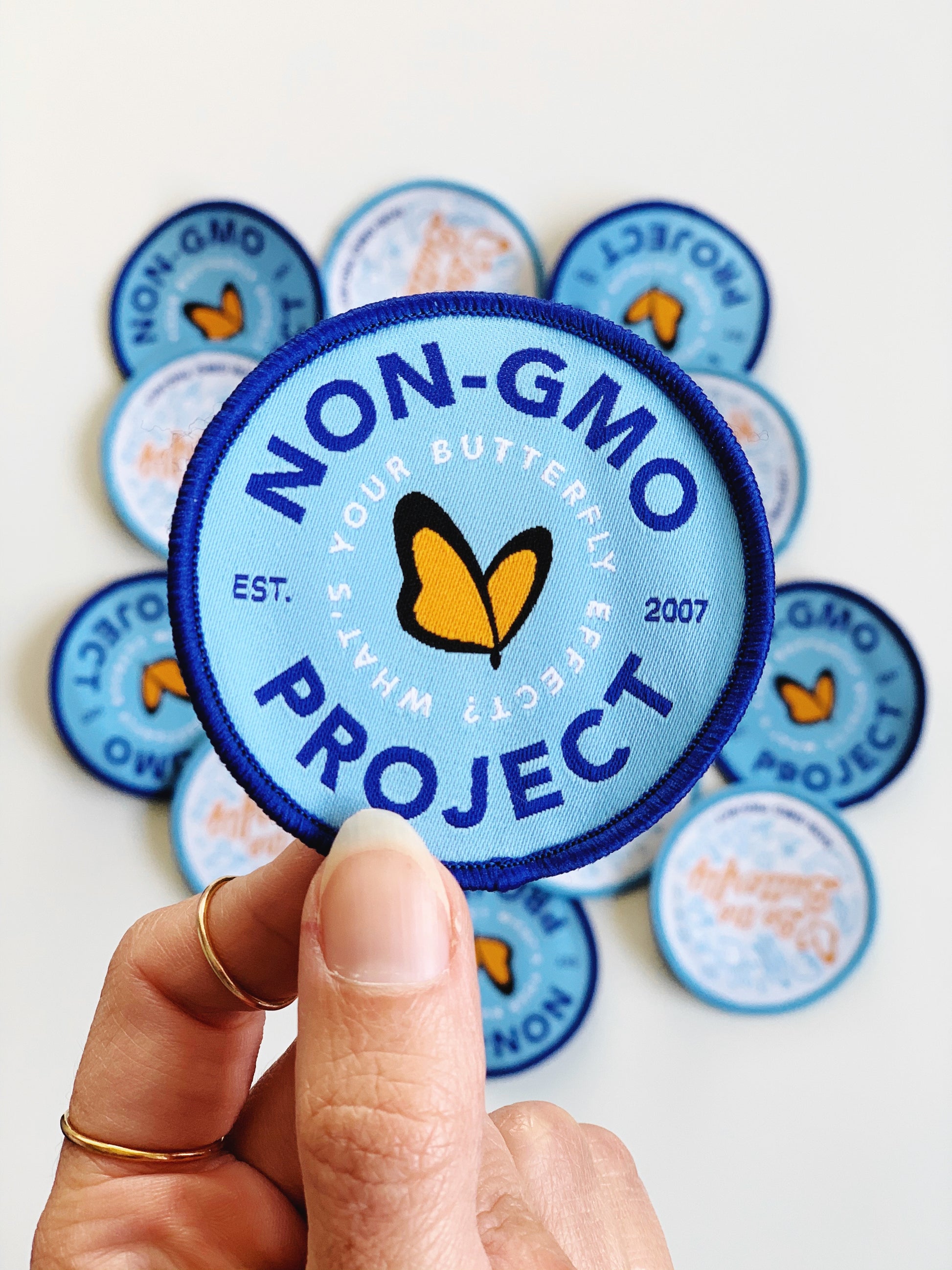 Group of Non-GMO Project patches, with in navy, light blue, and orange Non-GMO Project patch in focus